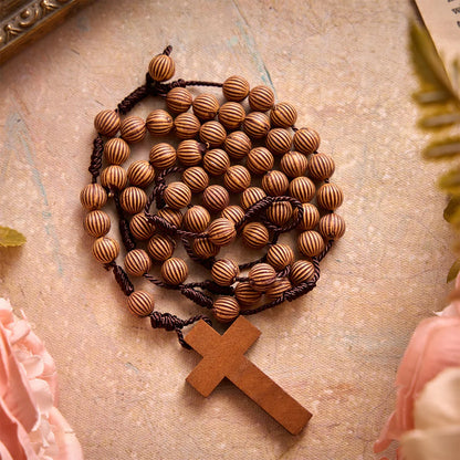 Pleciony różaniec z ciemnego sznurka z imitacji drewna z zawieszką w kształcie krzyża: symbol mało wymagającej ozdoby religijnej